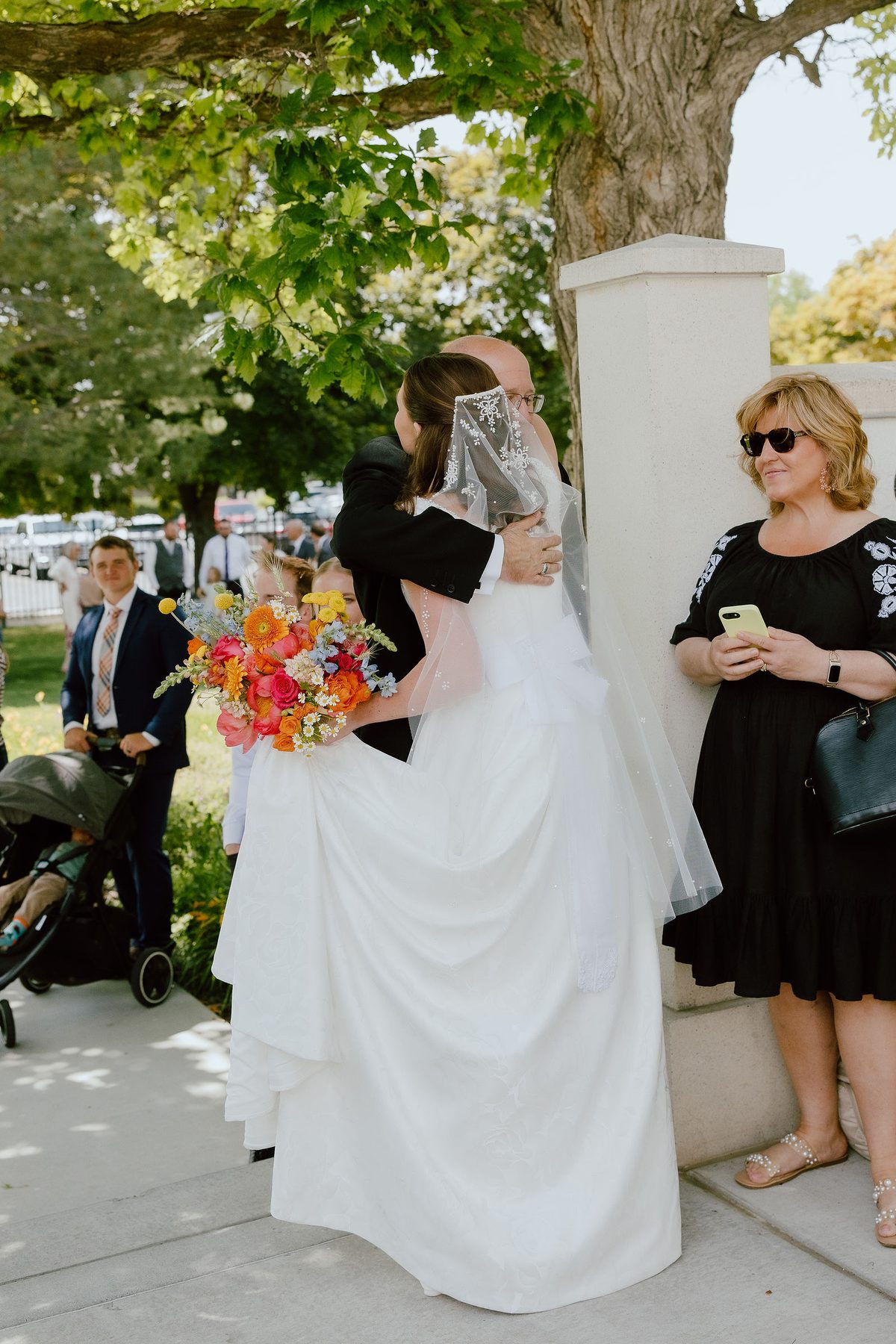 A bride seen from behind in a veil and full skirt, holding a bright bouquet